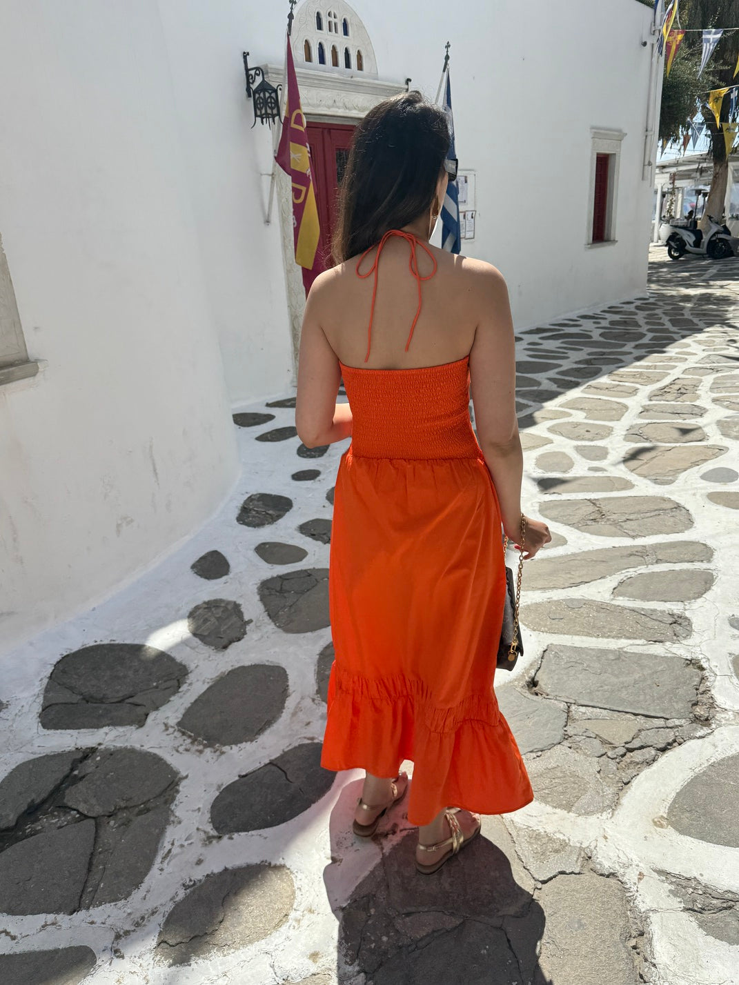 Person wearing an orange dress on a stone pavement with a white building in the background